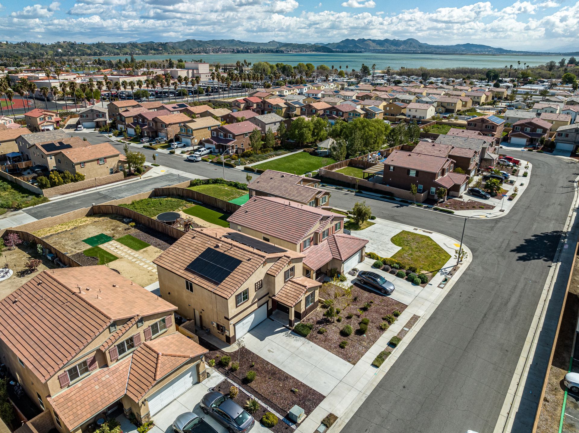 Aerial view of a suburban neighborhood with tan-roofed houses, streets, and distant hills under a clear sky
