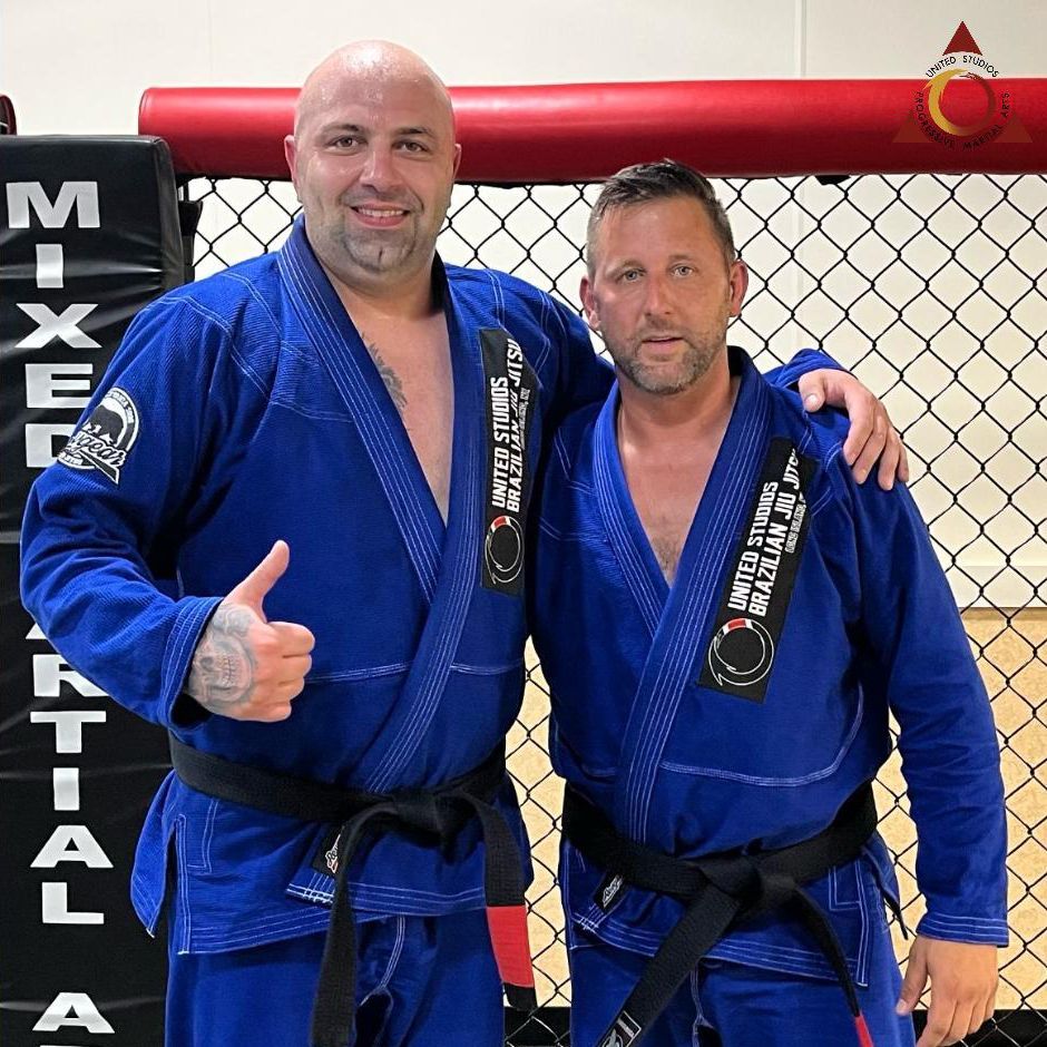 Two men are posing for a picture in front of a mixed martial arts cage