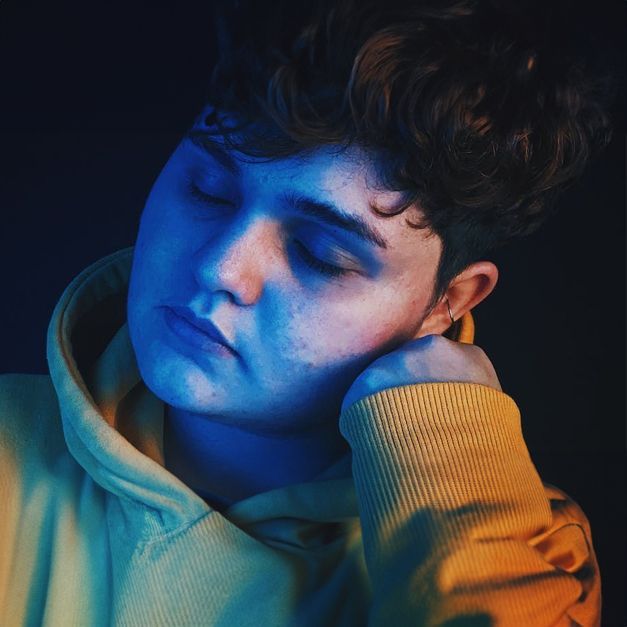 A young man in a yellow hoodie is sleeping with his eyes closed.