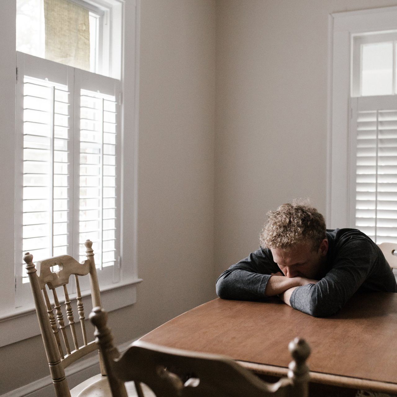 A man is sitting at a table with his head resting on his hands.