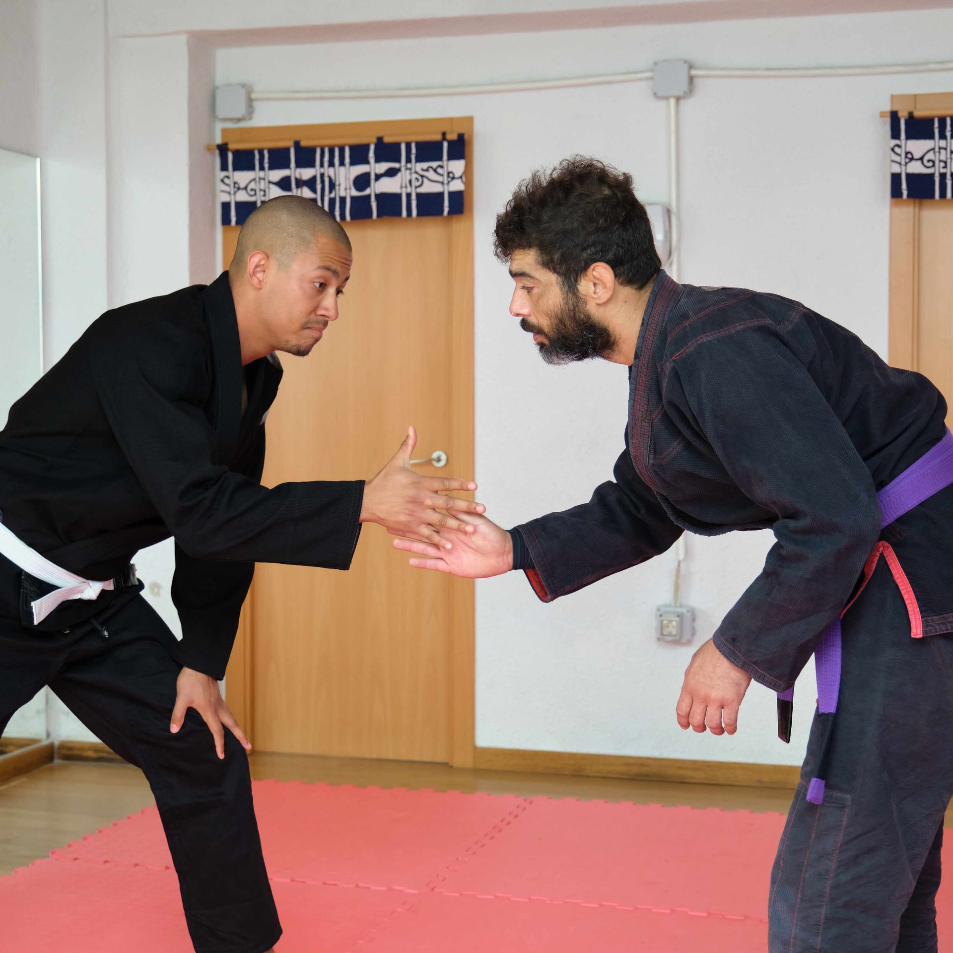 Two men in black karate uniforms are wrestling on a mat