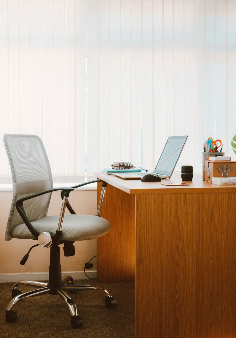 Office desk with laptop, chair, and window blinds.