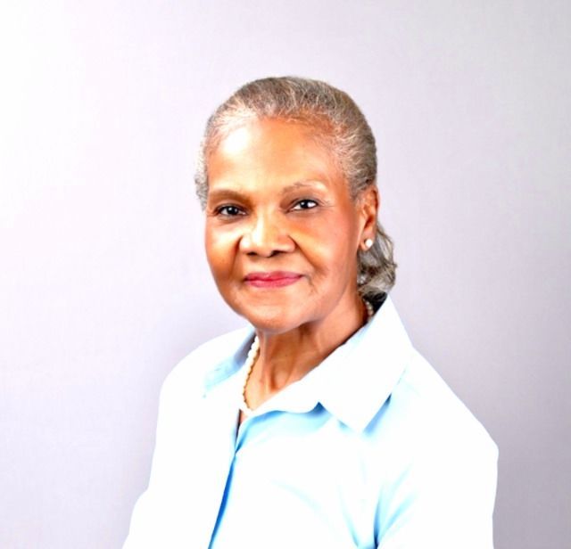 Portrait of a smiling woman in a light blue shirt against a soft gray background