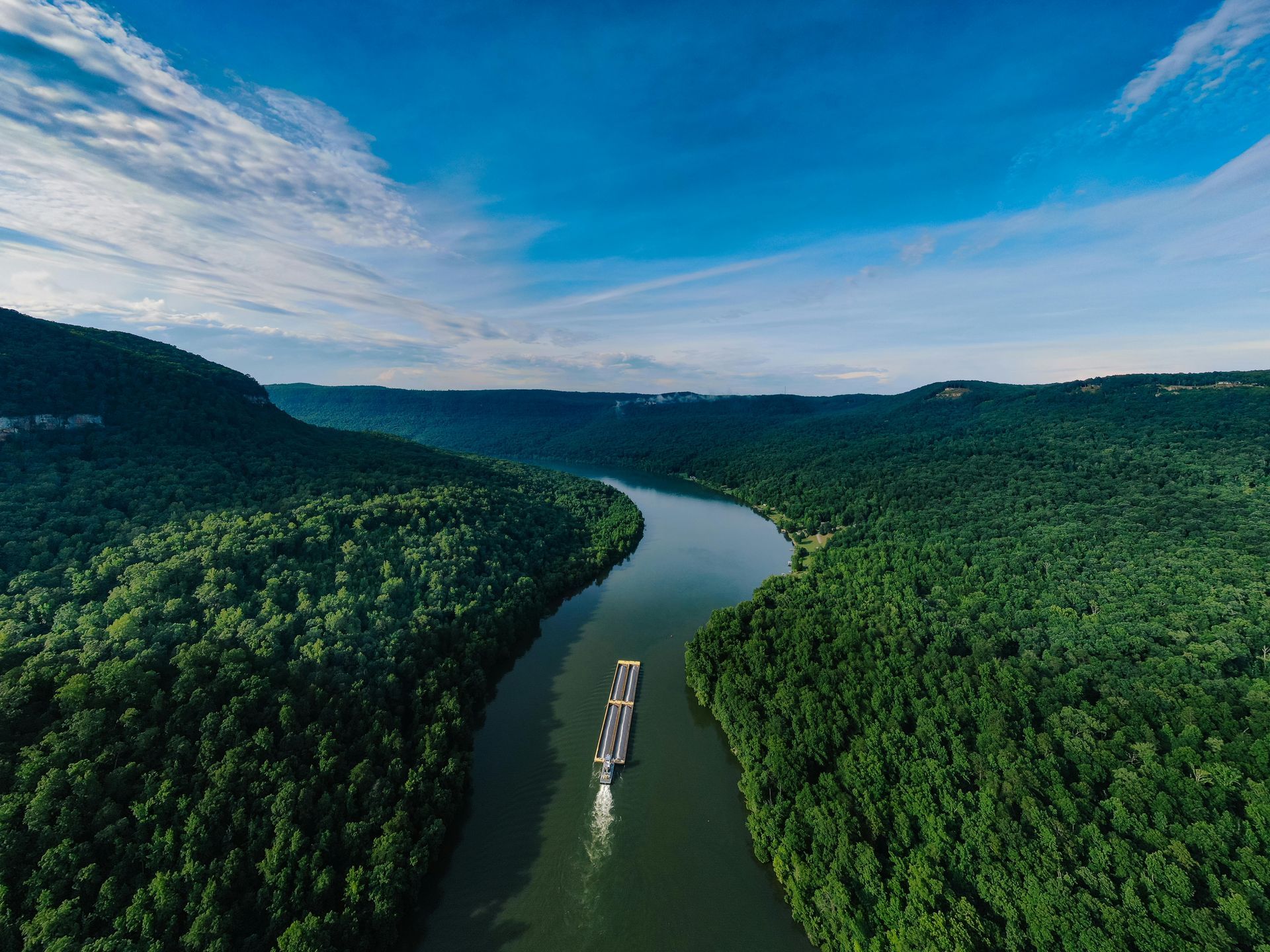 Aerial view of a winding river through dense green forest under a blue sky