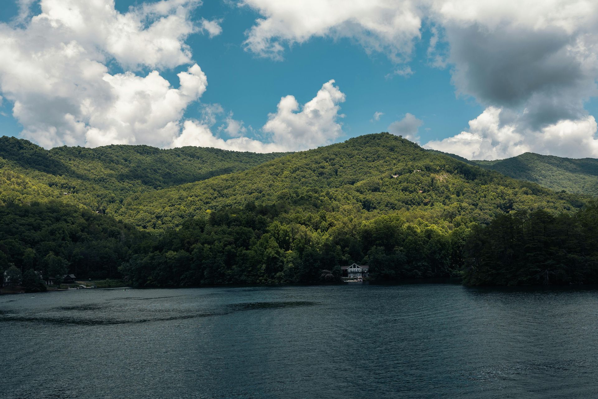 Forested mountains above a calm lake under a cloudy blue sky