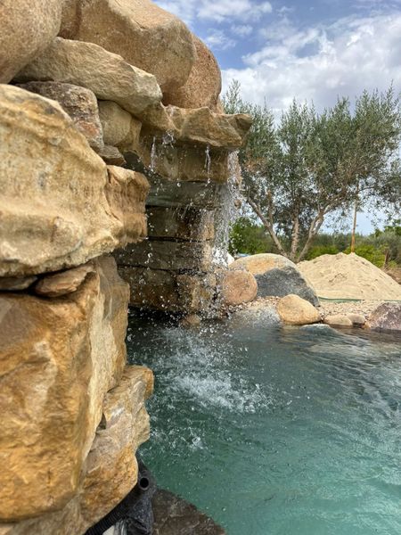 Una cascata si riversa su rocce color ocra in una pozza blu, con alberi sullo sfondo.
