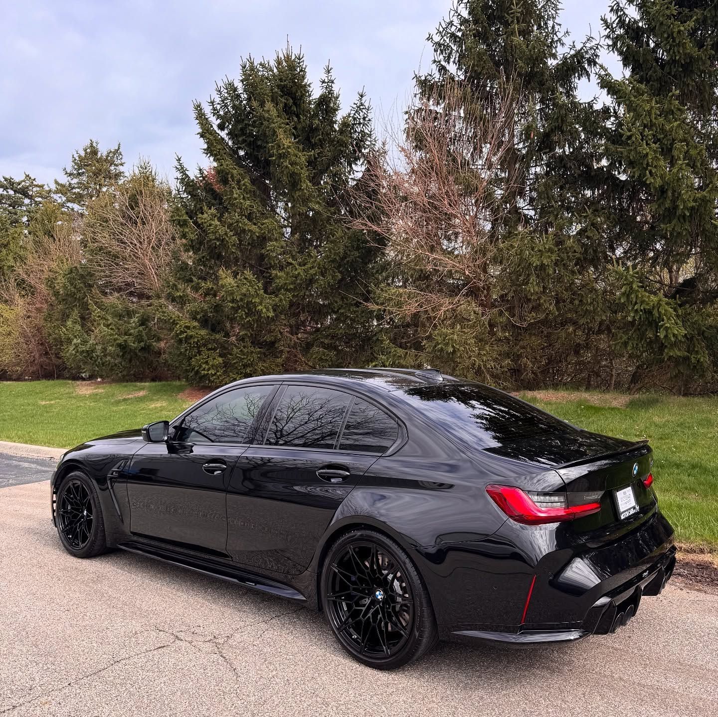 Black BMW sedan parked on pavement with trees in the background.