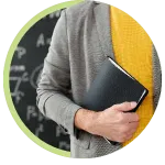 Person in gray sweater holding a black notebook in front of a chalkboard
