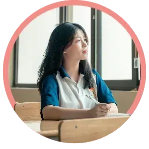 Student sitting at a classroom desk by a window, looking outside with a pen in hand