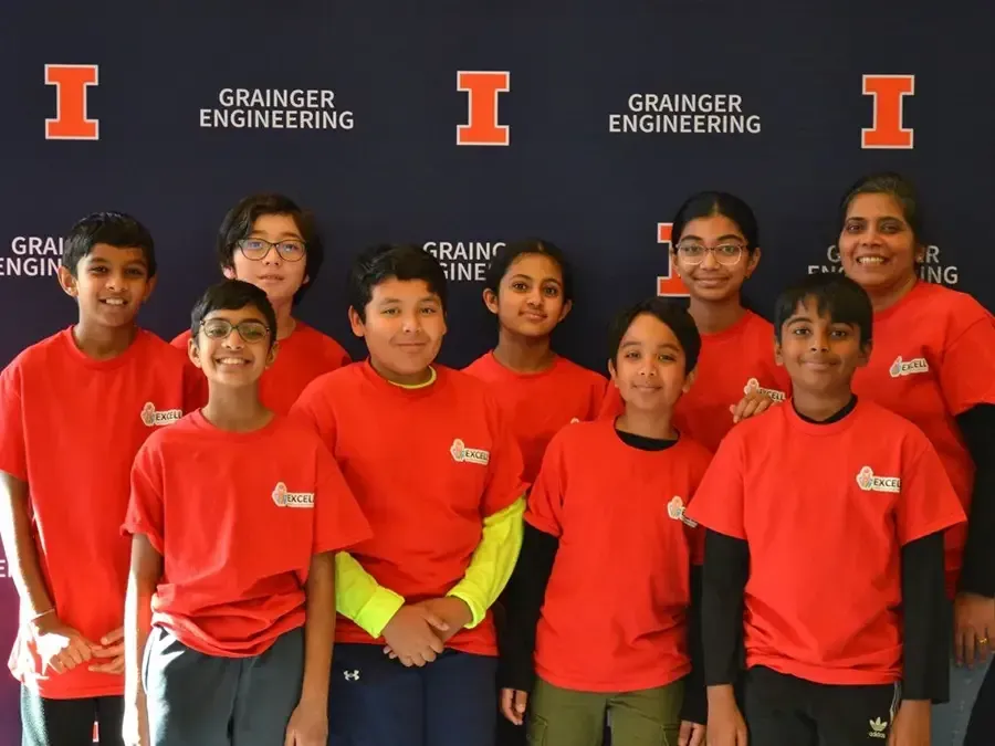 Group of students in red shirts posing in front of an Illinois Grainger Engineering backdrop