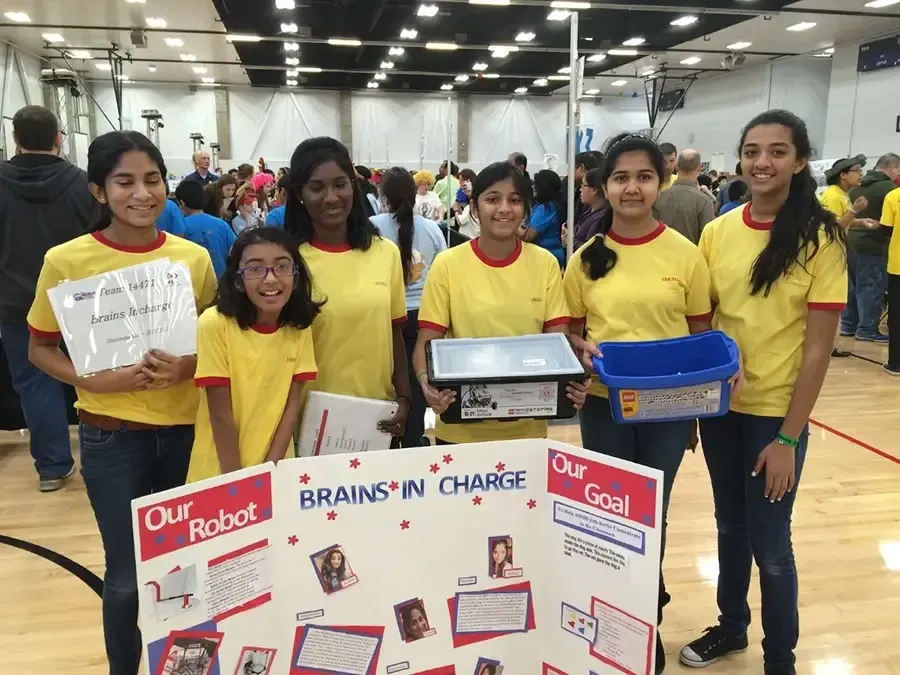 Students in yellow shirts hold recycling posters and bins at an indoor event.