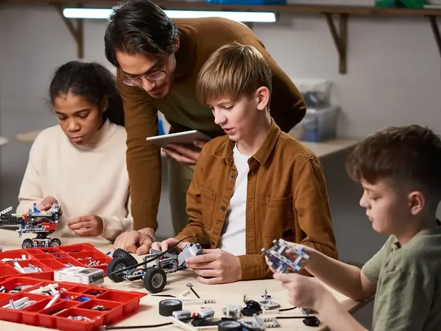 People assembling small robots at a worktable with tools and parts