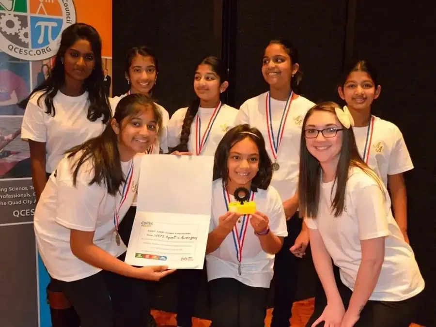 Group of students in white shirts posing with a certificate and medals at an award ceremony