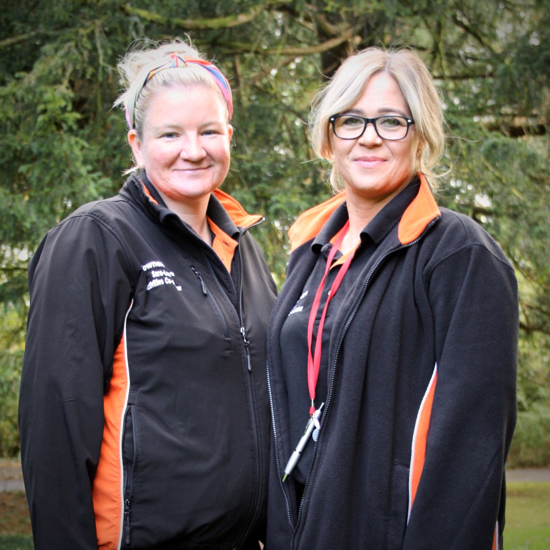 Two women wearing black and orange jackets are posing for a picture