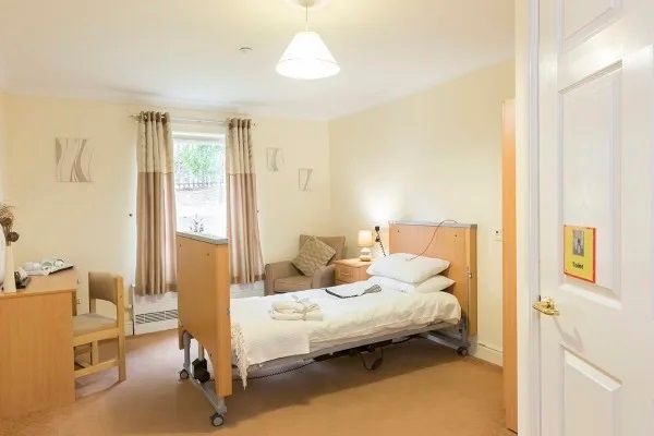 A nursing home bedroom with a hospital bed, chair, and desk.