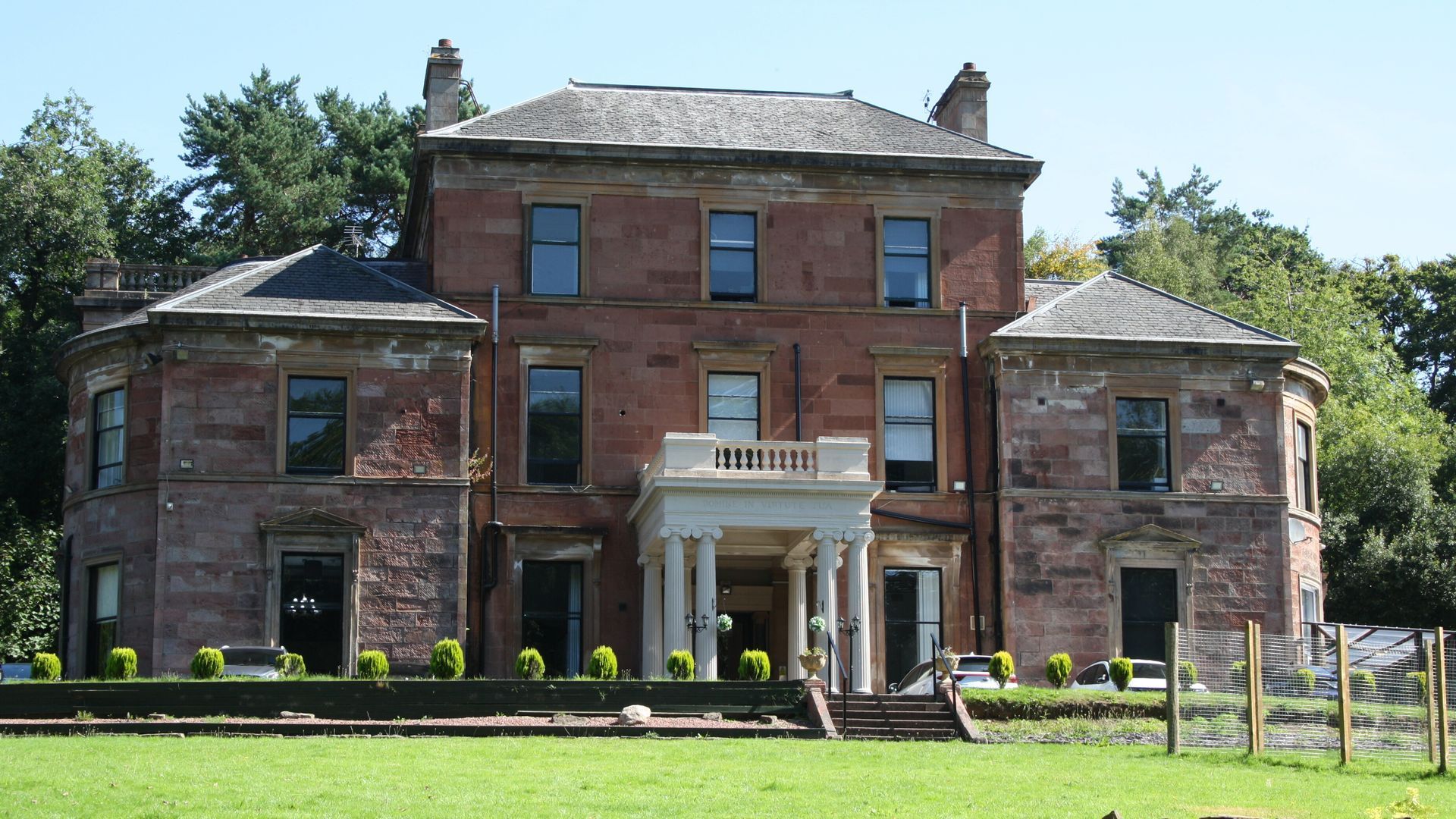Calderglen House. Red brick mansion with white columns, a gray roof, and a green lawn.