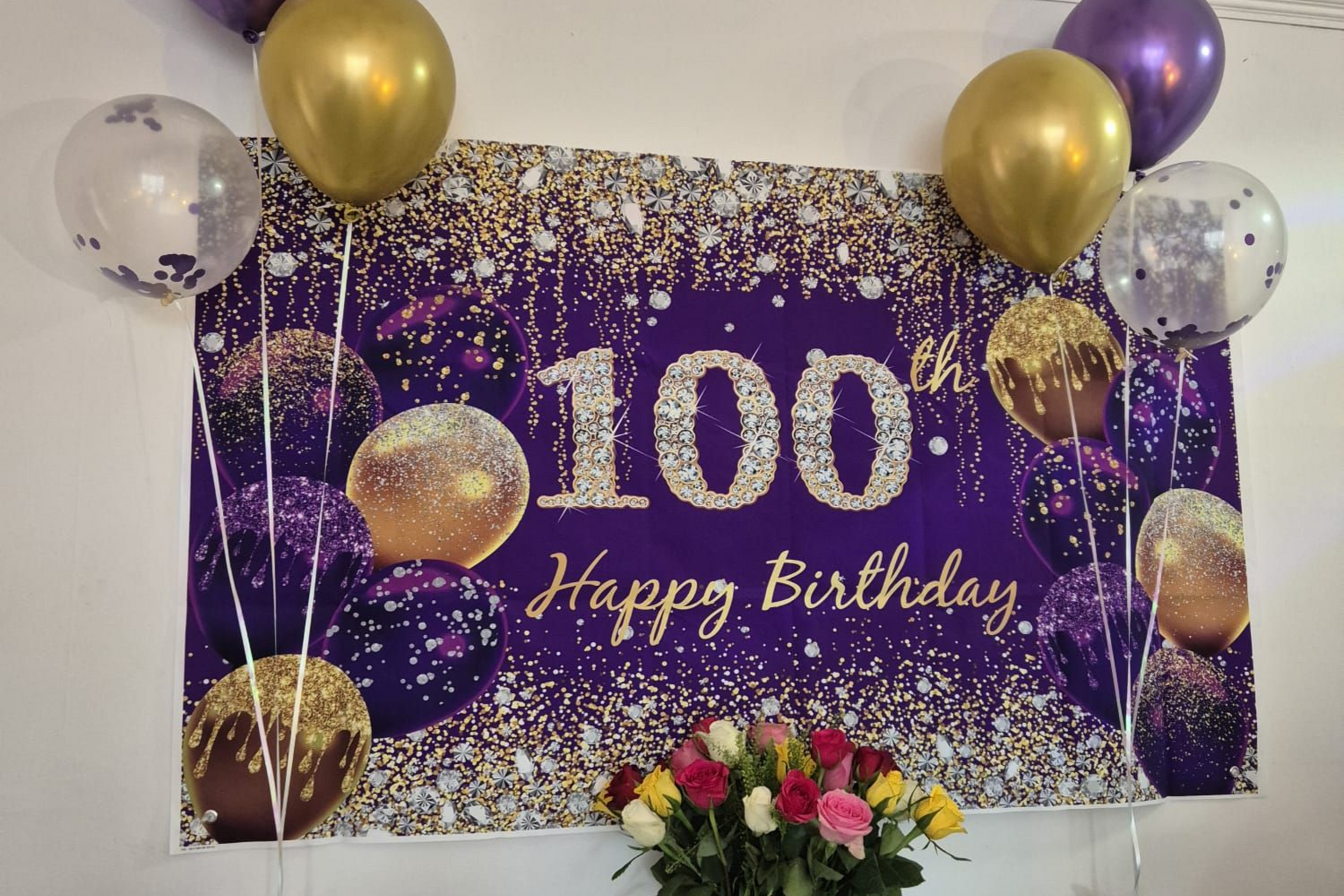 Elderly woman with tiara smiles, holding cake with 