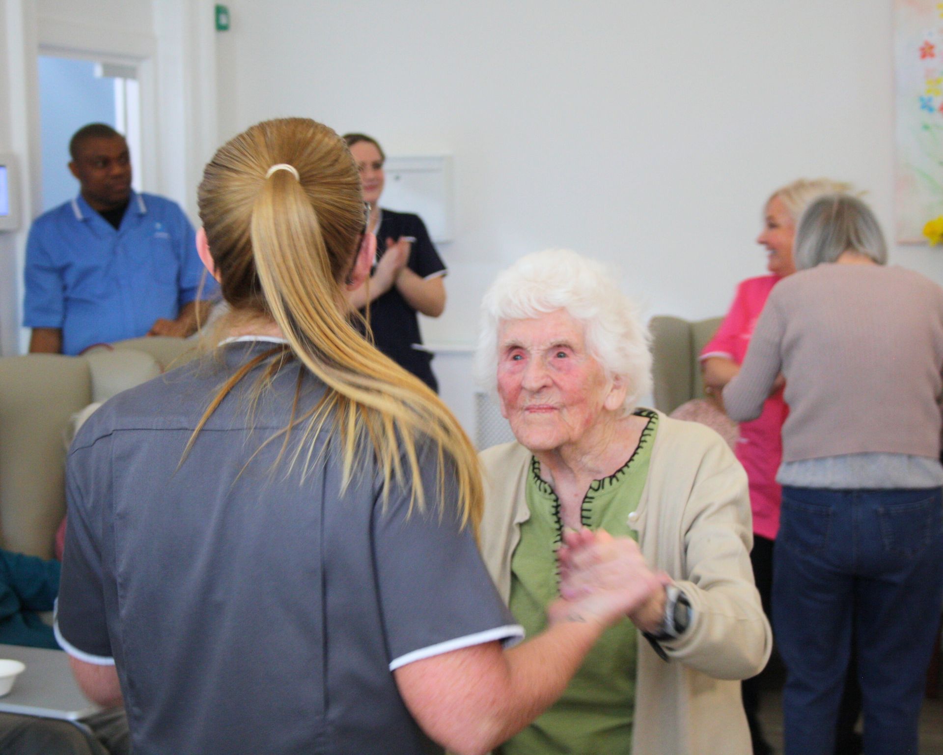 An elderly woman is dancing with a nurse in a nursing home