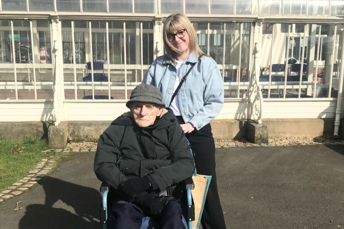 A woman is standing next to a man in a wheelchair.