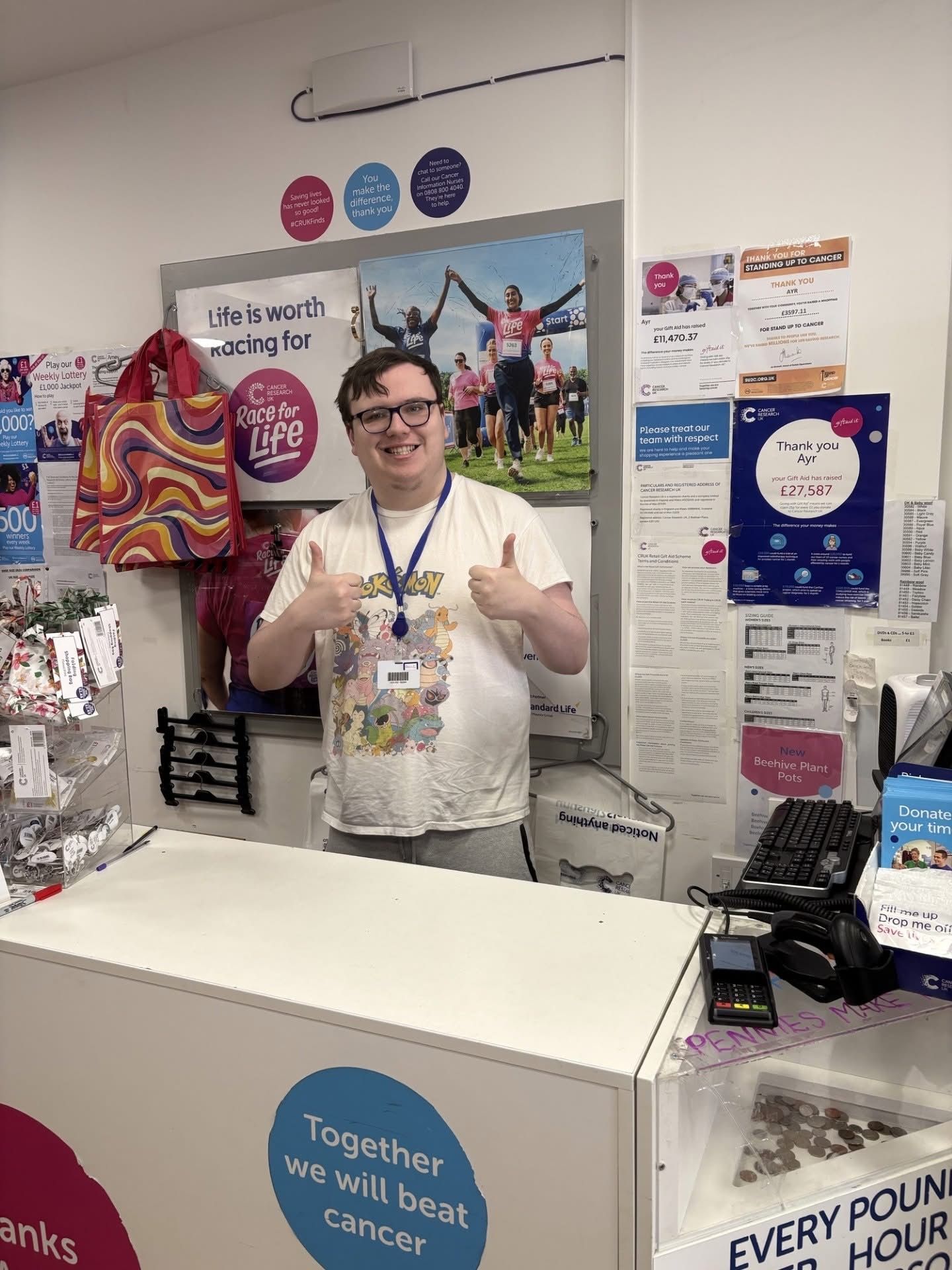 A man is standing behind a counter in a store giving a thumbs up.