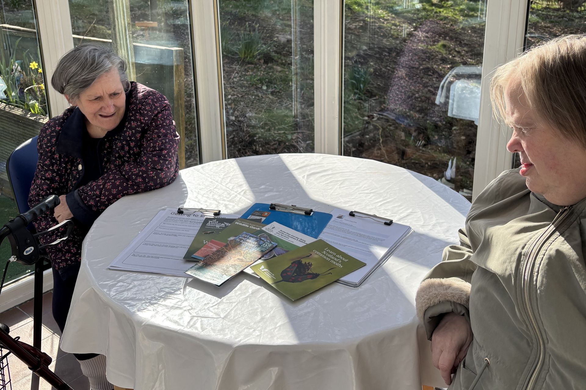 Two women are sitting at a table with books on it.