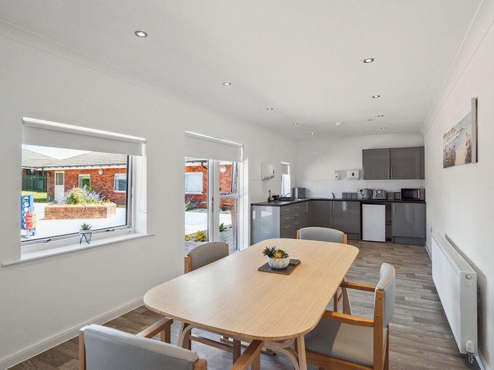 A dining room with a table and chairs and a kitchen in the background at Arran View