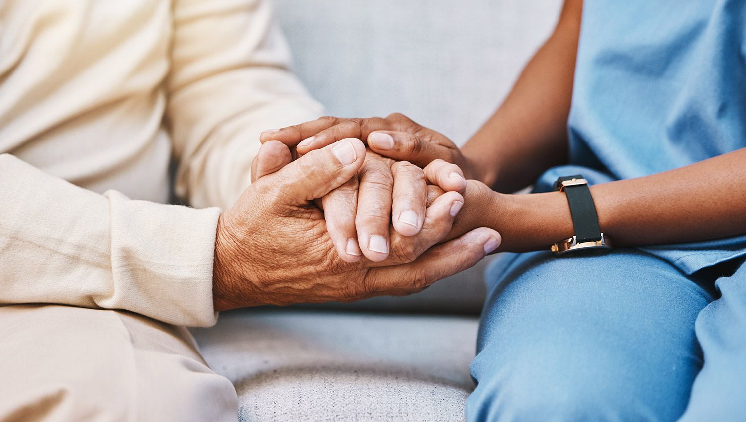 A nurse is holding the hands of an elderly woman.
