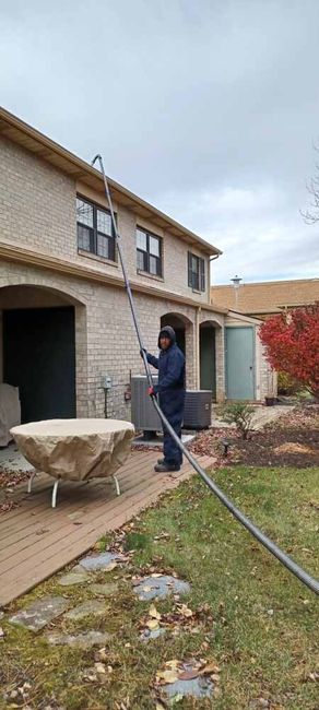 Worker power-washing a two-story house exterior beside a patio and lawn