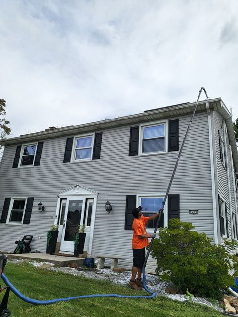 Worker in an orange shirt power-washing a two-story house’s siding near the front entry.