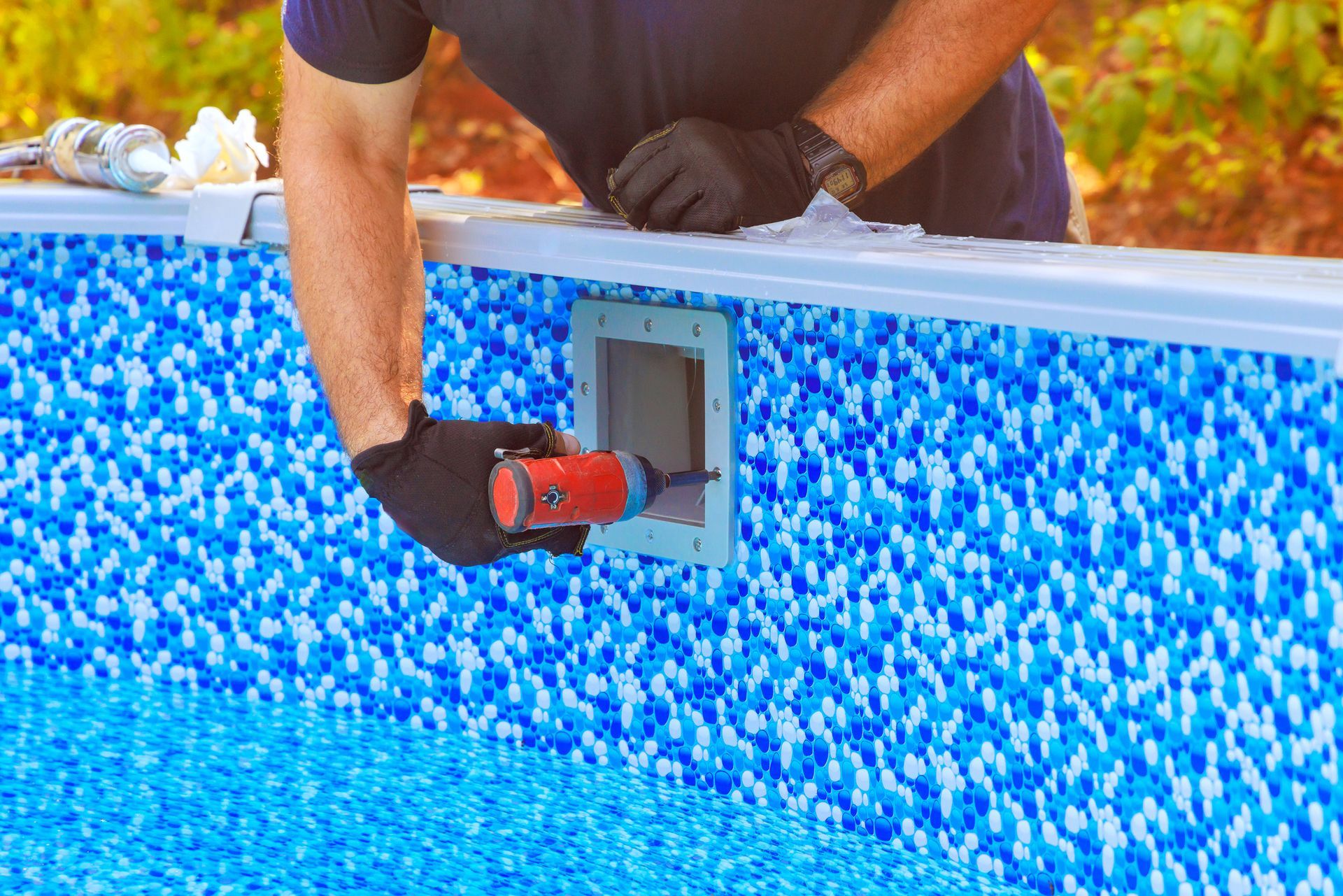 Gloved hands apply sealant to pool skimmer on mosaic wall. Gloved hands apply sealant to pool skimmer on mosaic wall.