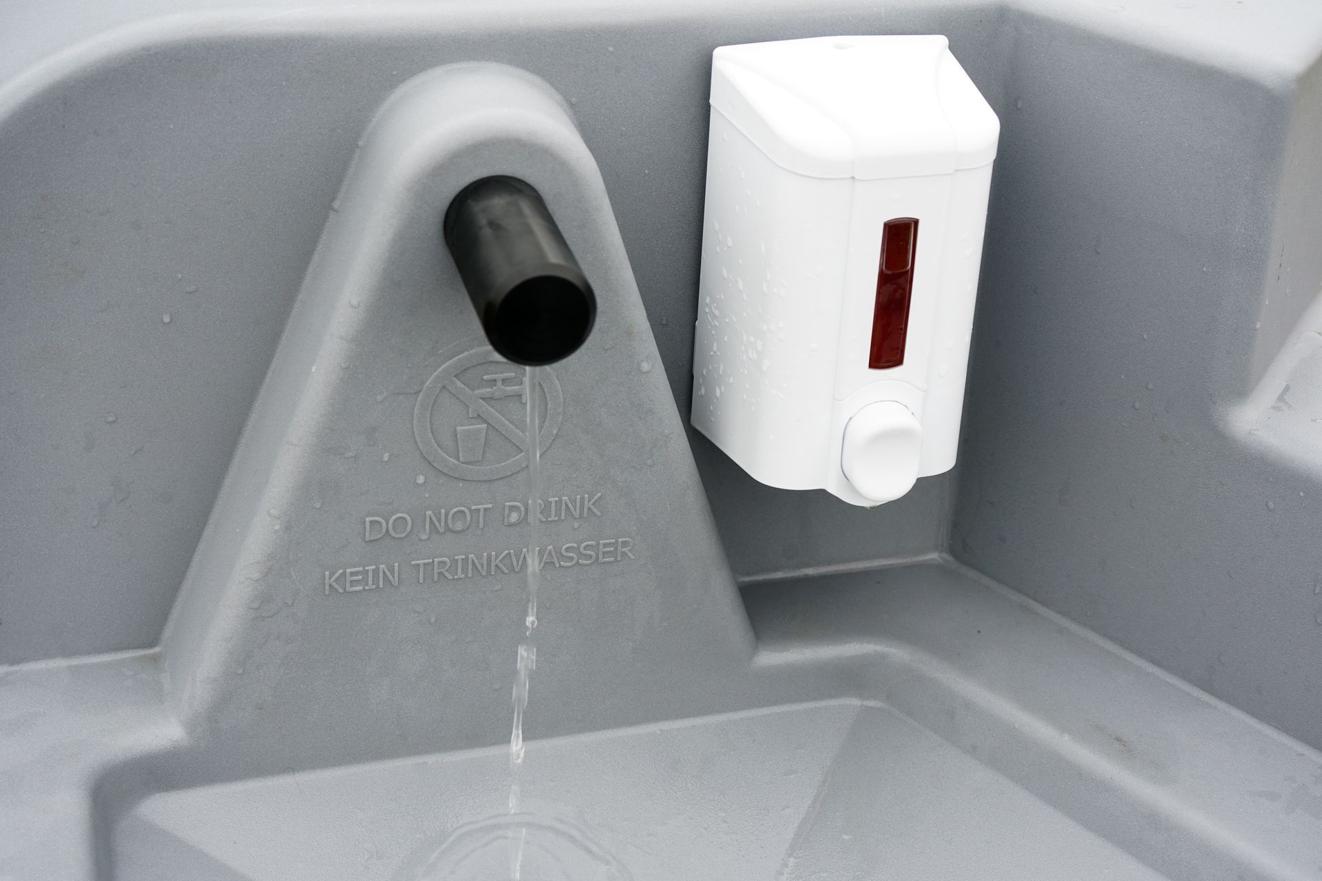 A grey plastic portable sink with a black water spout and a white soap dispenser mounted on the side.