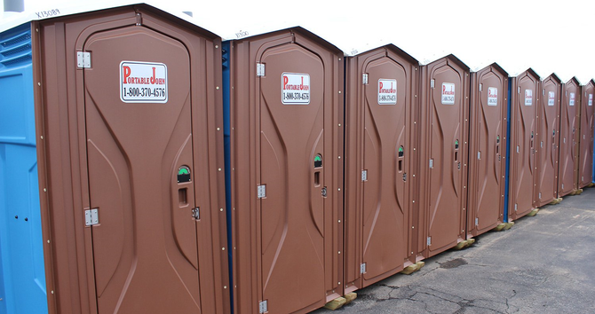 Four blue portable toilets standing in a row on a concrete sidewalk. Four blue portable toilets standing in a row on a concrete sidewalk.