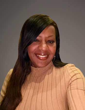 Smiling person with long dark hair wearing a beige sweater against a gray background