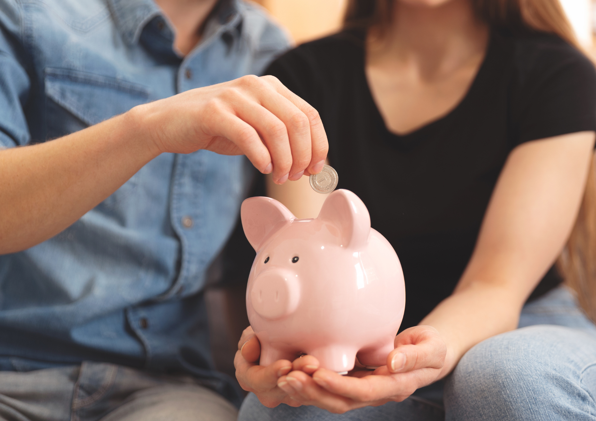 Two people saving money by placing coins into a piggy bank for future travel.