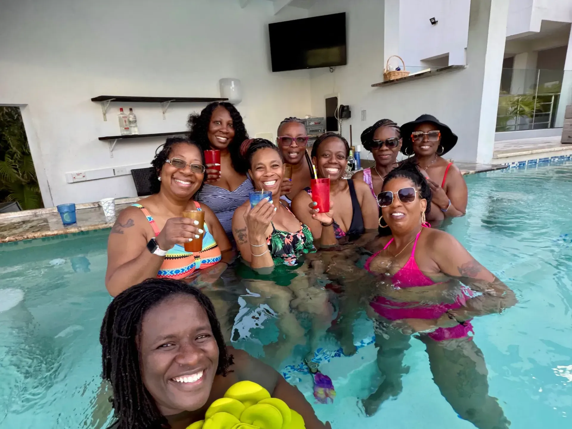 Group smiling in a pool, posing with drinks at a poolside gathering