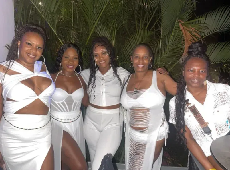Five people in white outfits pose together outdoors at night in front of palm leaves.