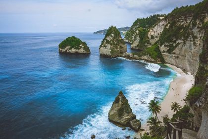 Blue ocean cove with steep cliffs, sandy beach, and rock formations under a bright sky