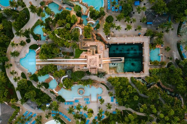 Aerial view of a tropical resort with a central pool, palm trees, and a lagoon-like water feature