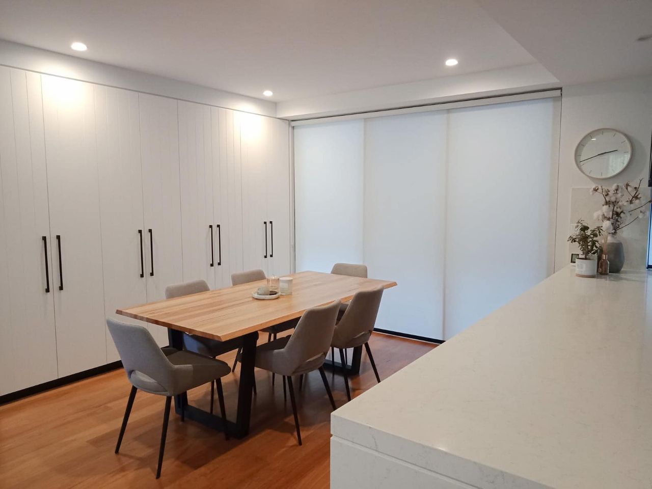 A Dining Room With A Table And Chairs And A Clock On The Wall — Ron Ayton Curtains, Blinds & Shutters In Avoca, NSW
