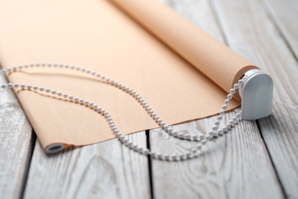 A Roll Of Blinds With A Chain On A Wooden Table — Ron Ayton Curtains, Blinds & Shutters In Shelly Beach, NSW