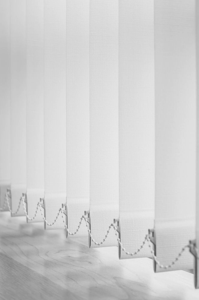 A Row Of White Vertical Blinds On A White Wall — Ron Ayton Curtains, Blinds & Shutters In Shelly Beach, NSW