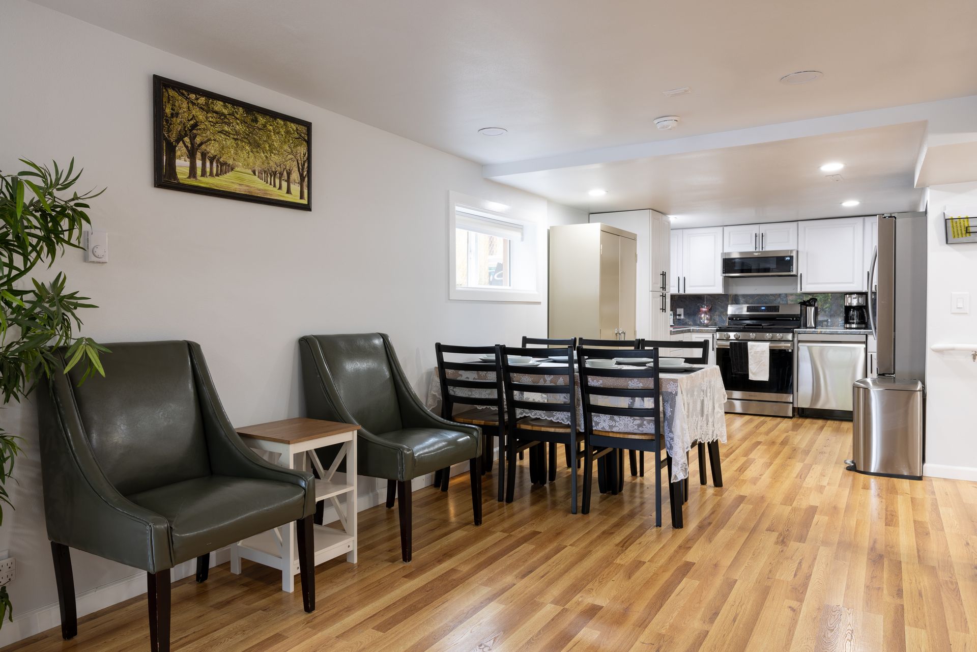 Open-concept dining and kitchen with wood floors, green chairs, and a dining table set.