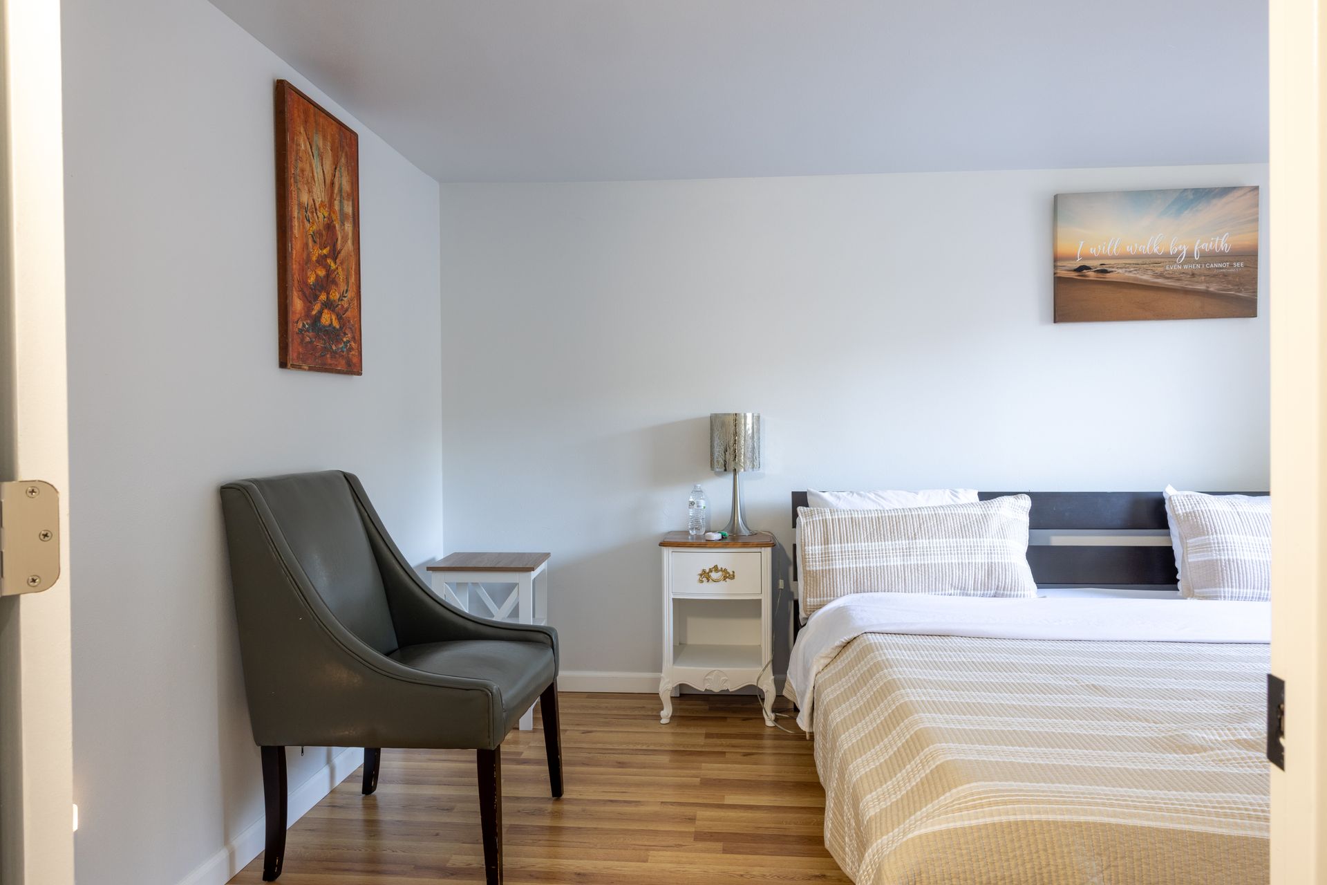 Bedroom interior with a bed, chair, and art on the wall.