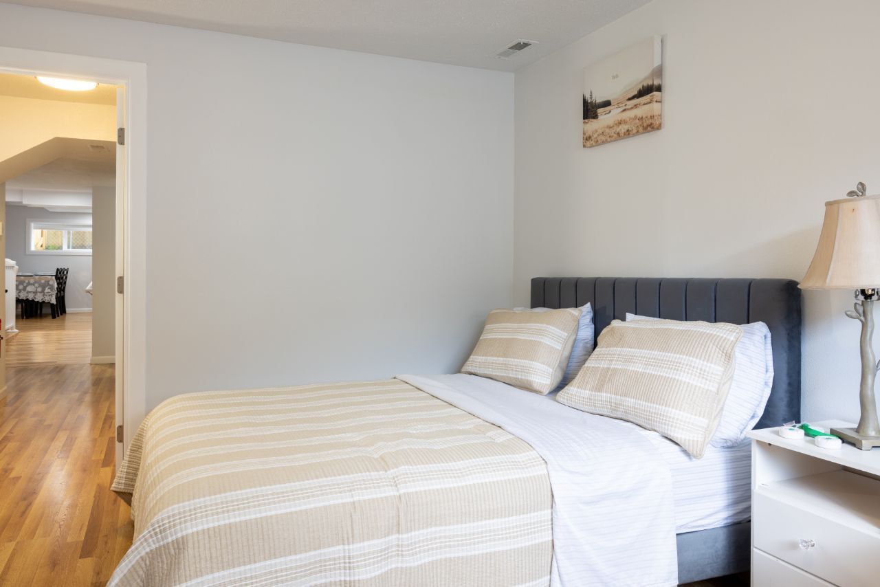 Bedroom with bed, pillows, lamp, and artwork; hallway visible.