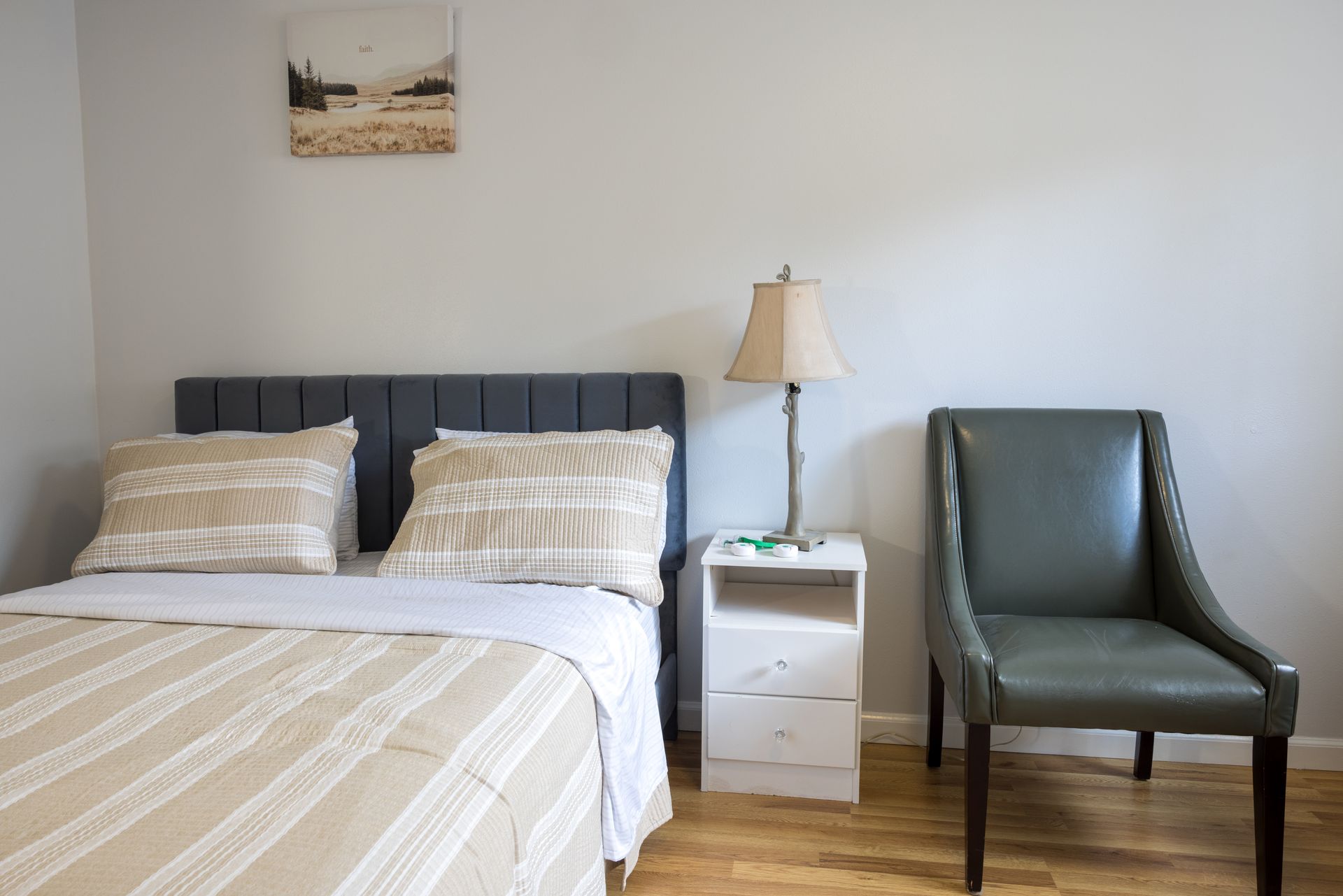 Bedroom with bed, nightstand, lamp, and chair. Gray and tan color scheme.