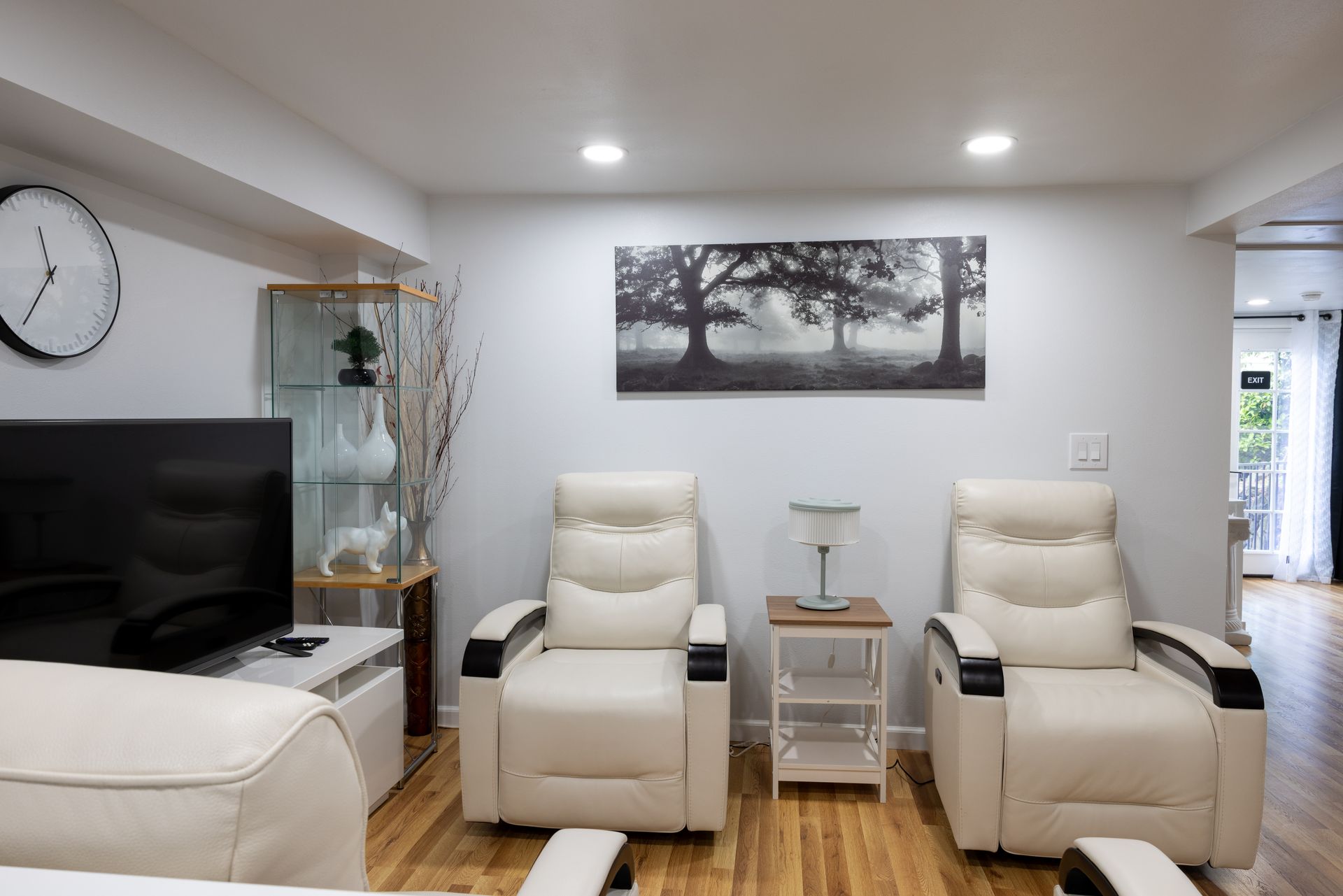 Living room with two cream recliners, a side table, artwork, a TV, and a glass cabinet.
