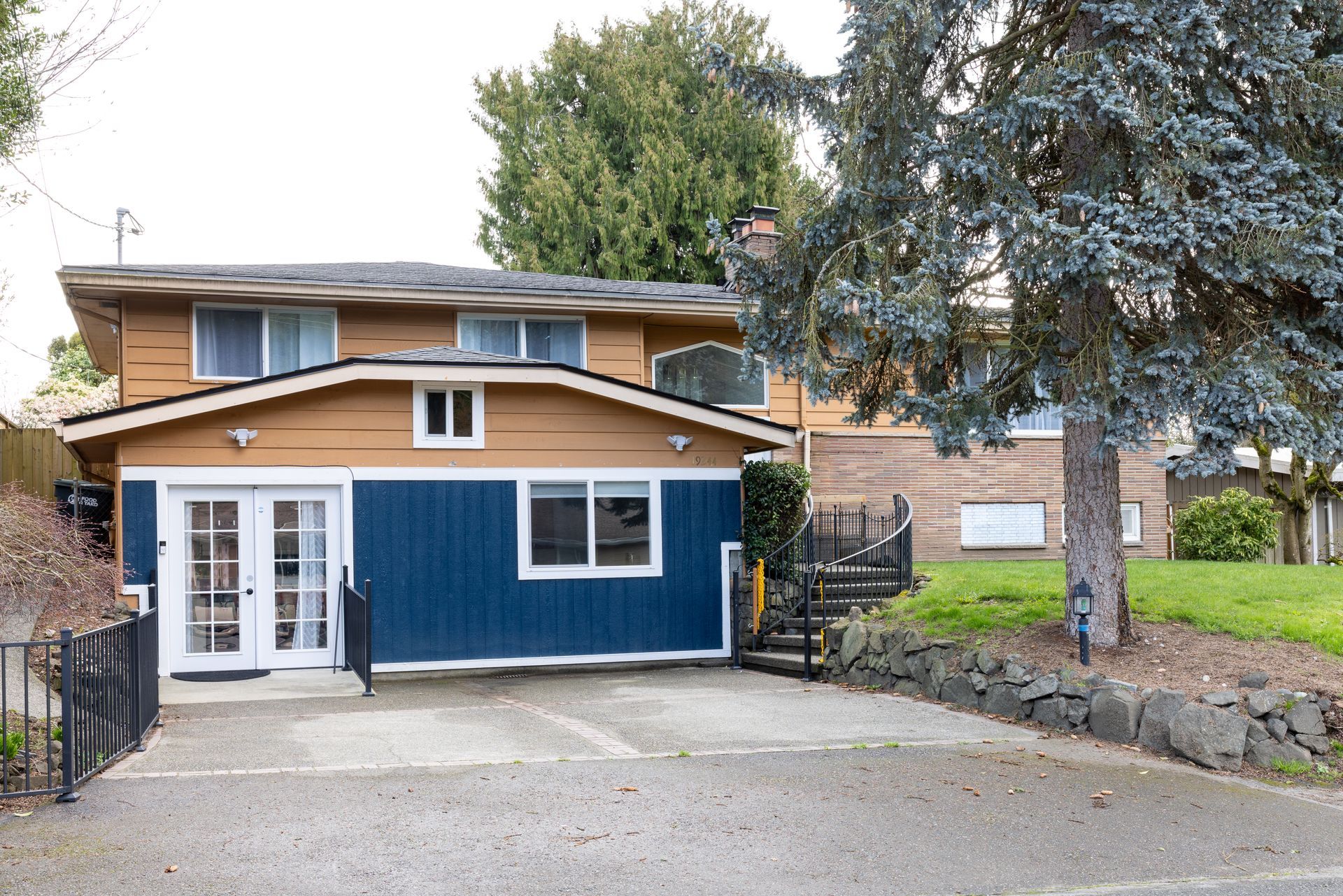 Two-story house with blue and tan siding, a driveway, and a tree in front.