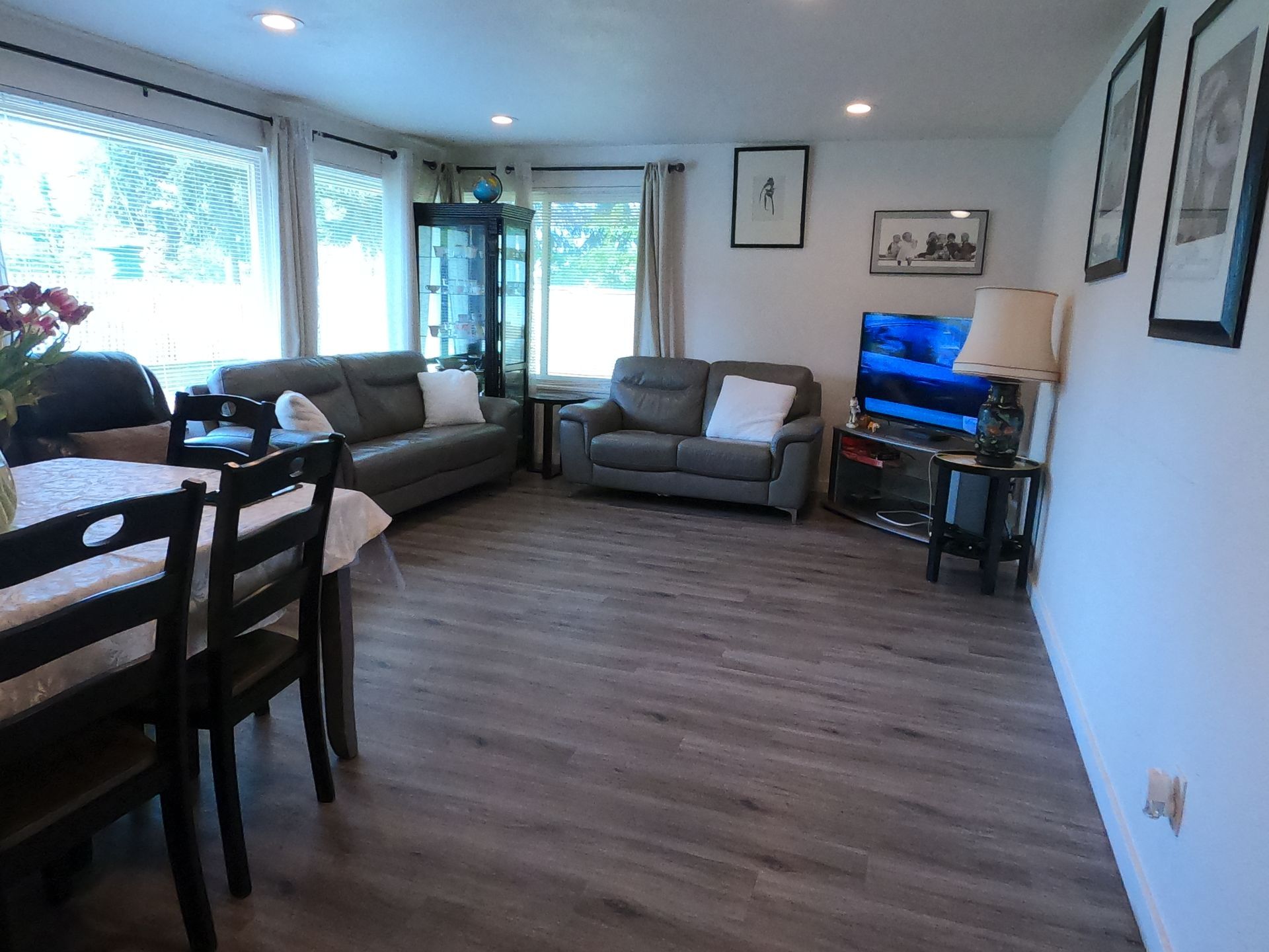 Living room with gray sofas, a dining table, and a TV. Light-colored walls and flooring.