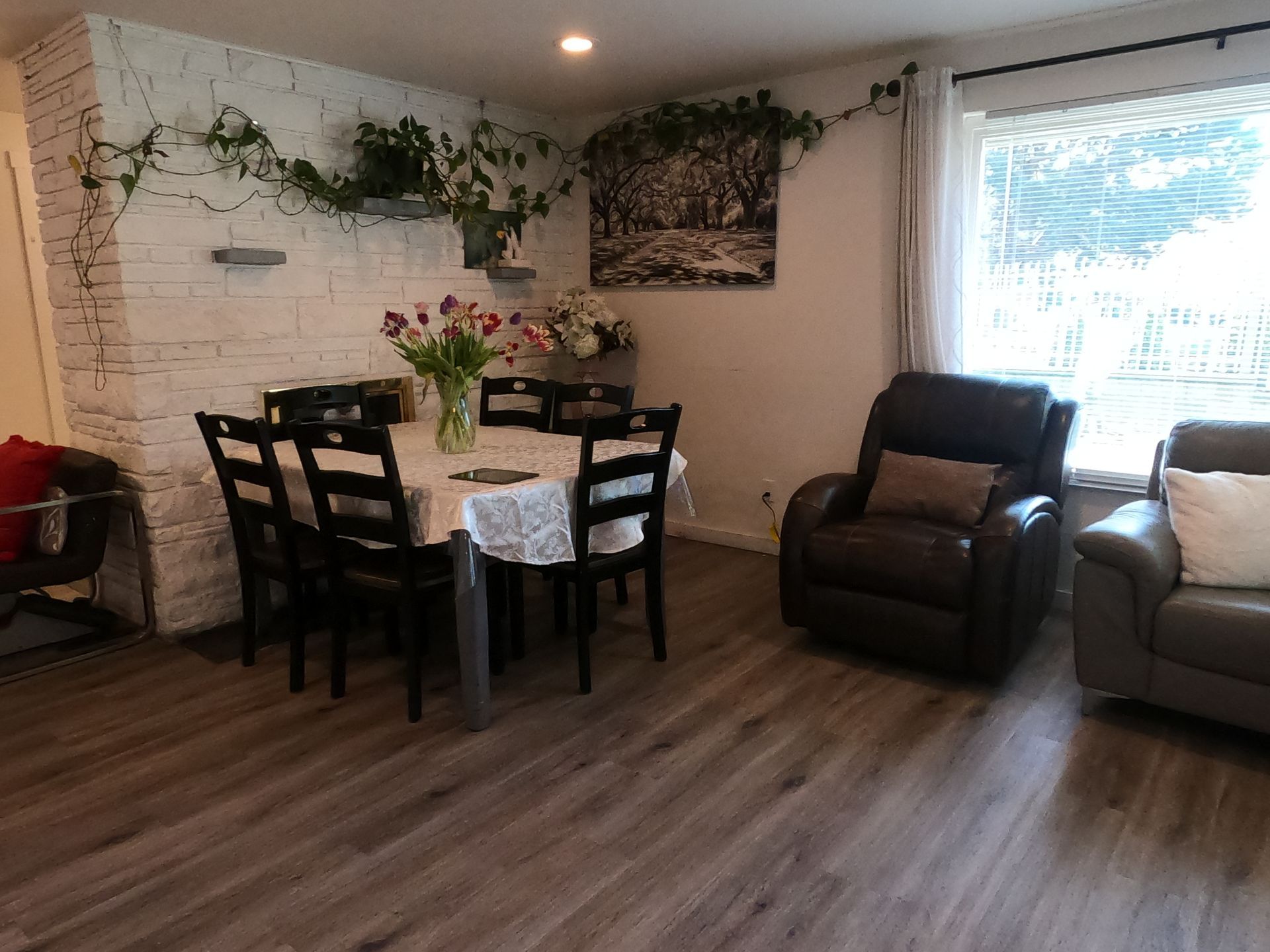 Dining area with white brick wall, table set for six, and two leather armchairs.
