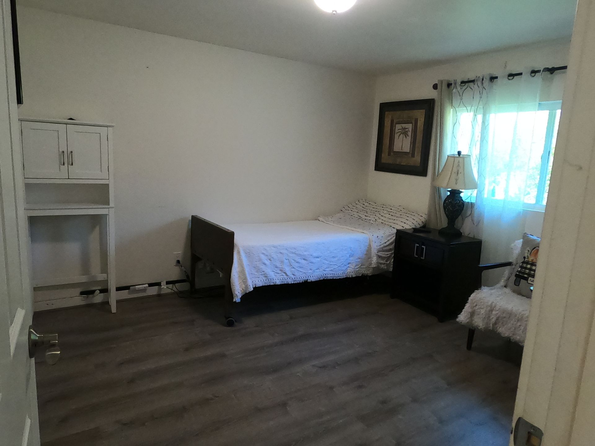 Bedroom with a white bed, dark nightstand, and small cabinet.